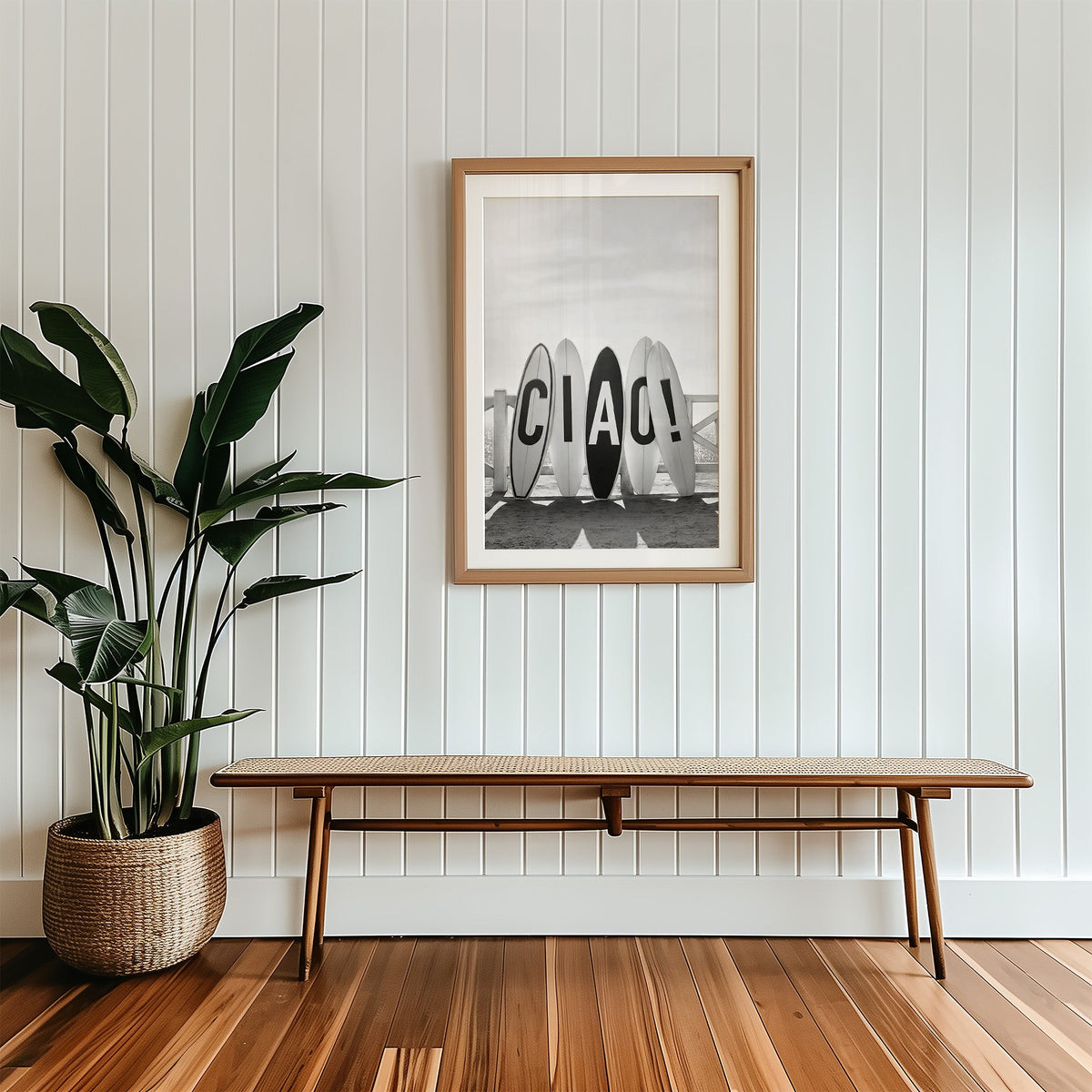 Five surfboards spelling CIAO by a beach fence print in a wood frame with a white mat above a cane bench
