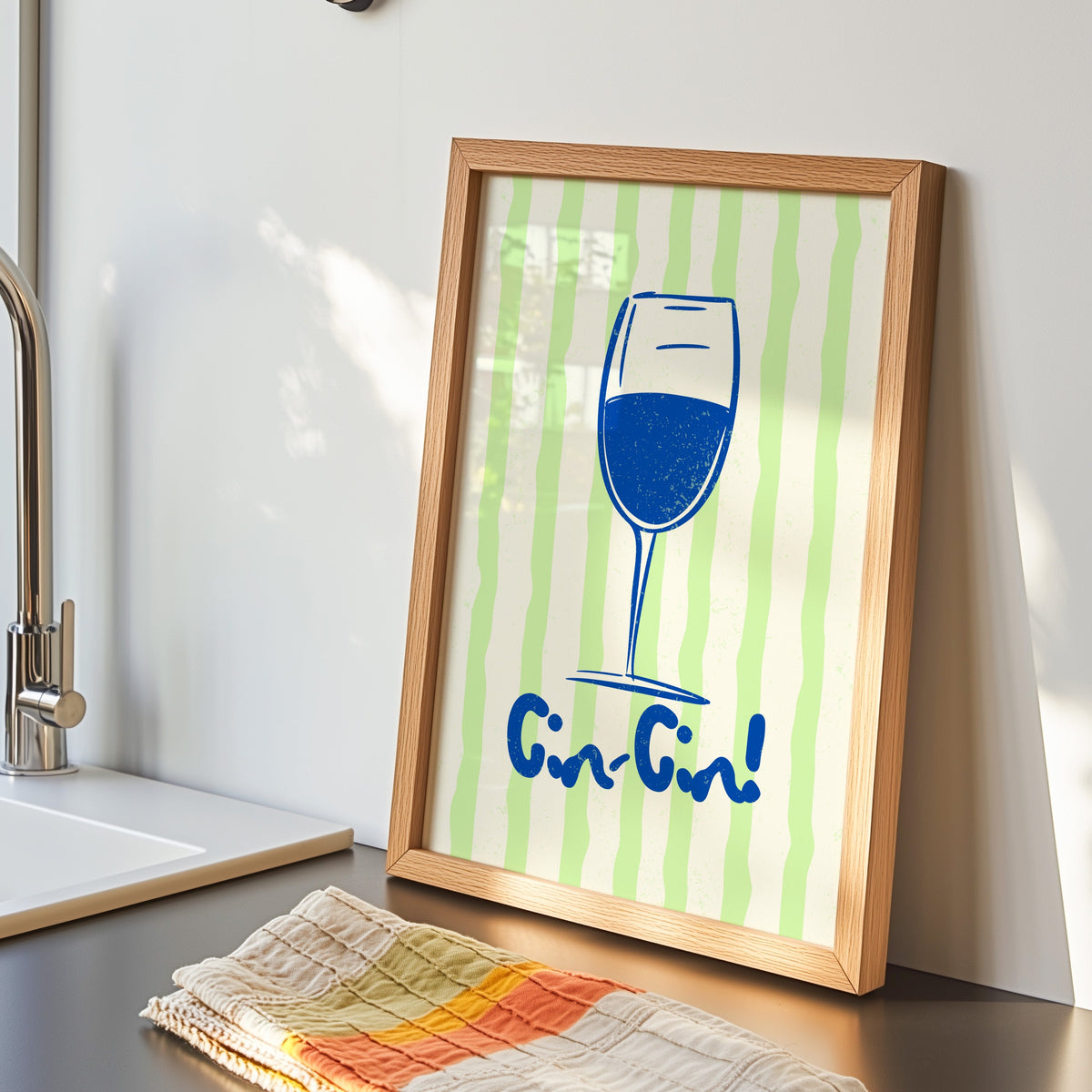 Cin Cin blue glass print in an oak frame by the kitchen sink beside a striped tea towel