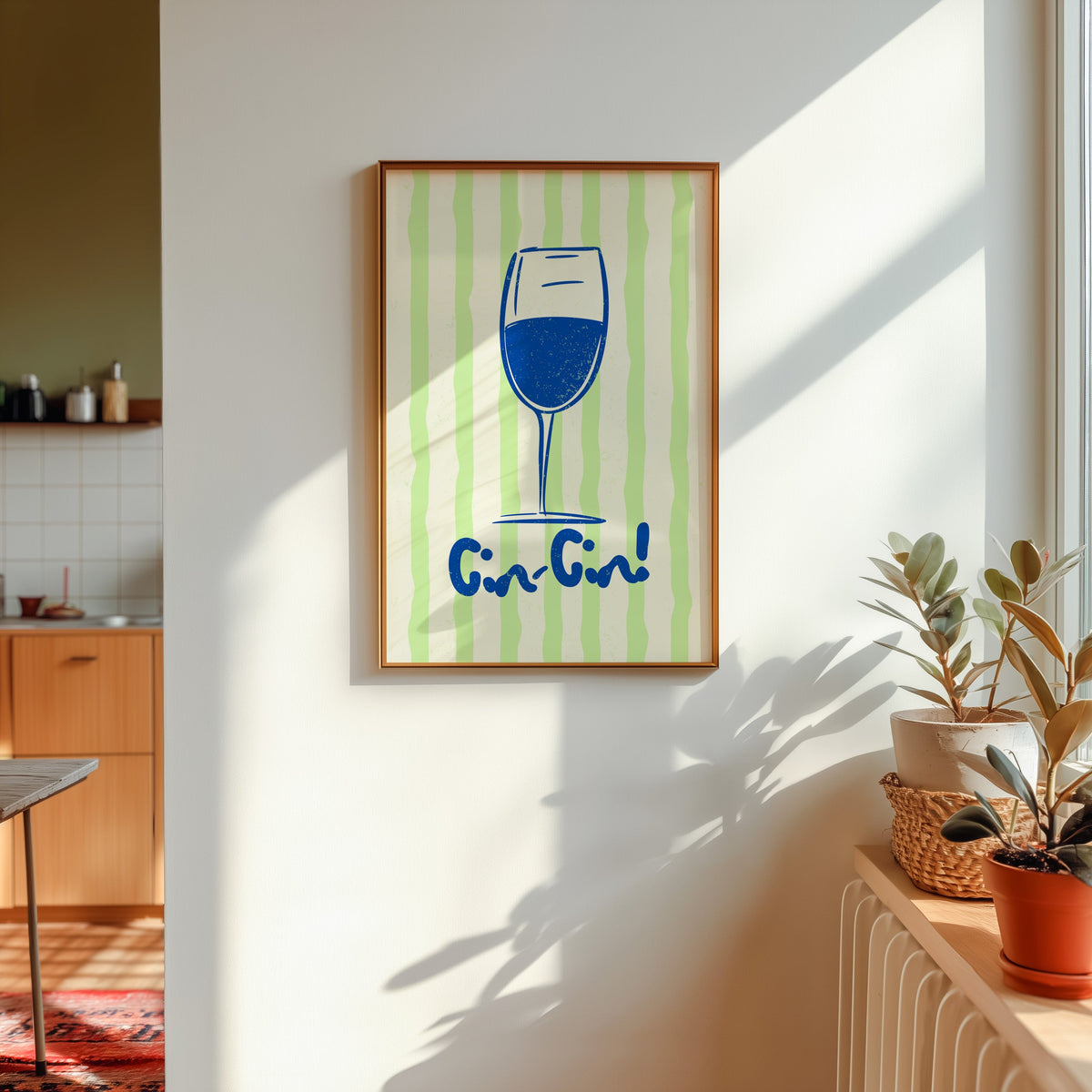 Cin Cin blue glass print shown in a gold frame in sunlight with plants and a kitchen beyond