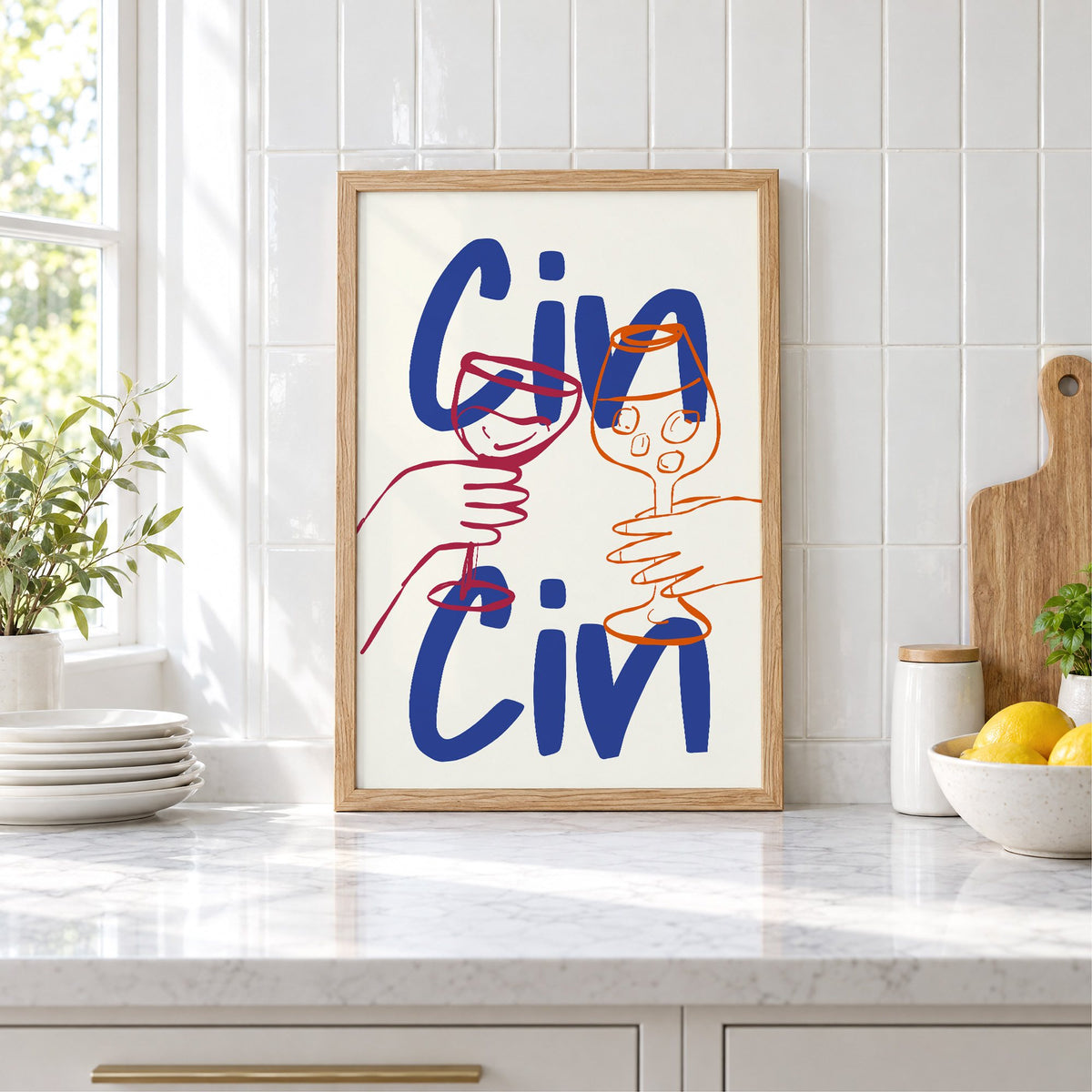 Cin Cin cobalt blue toast print in an oak frame leaning on a marble counter by white tiles and lemons