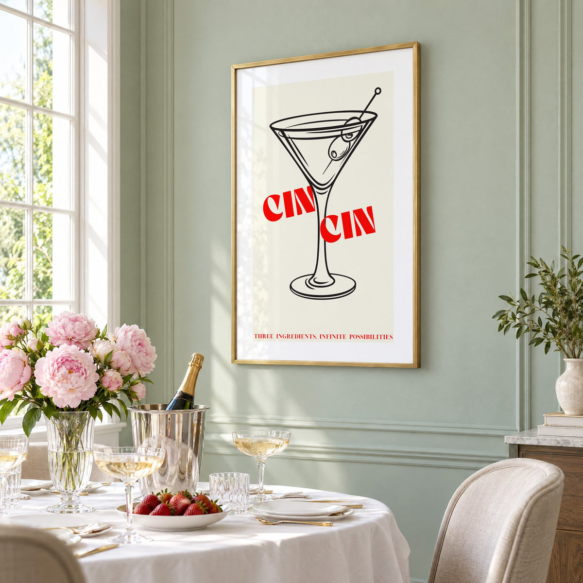 CIN CIN red type martini olives print in a brass frame on a sage wall above a brunch table with champagne and peonies, seen at an angle