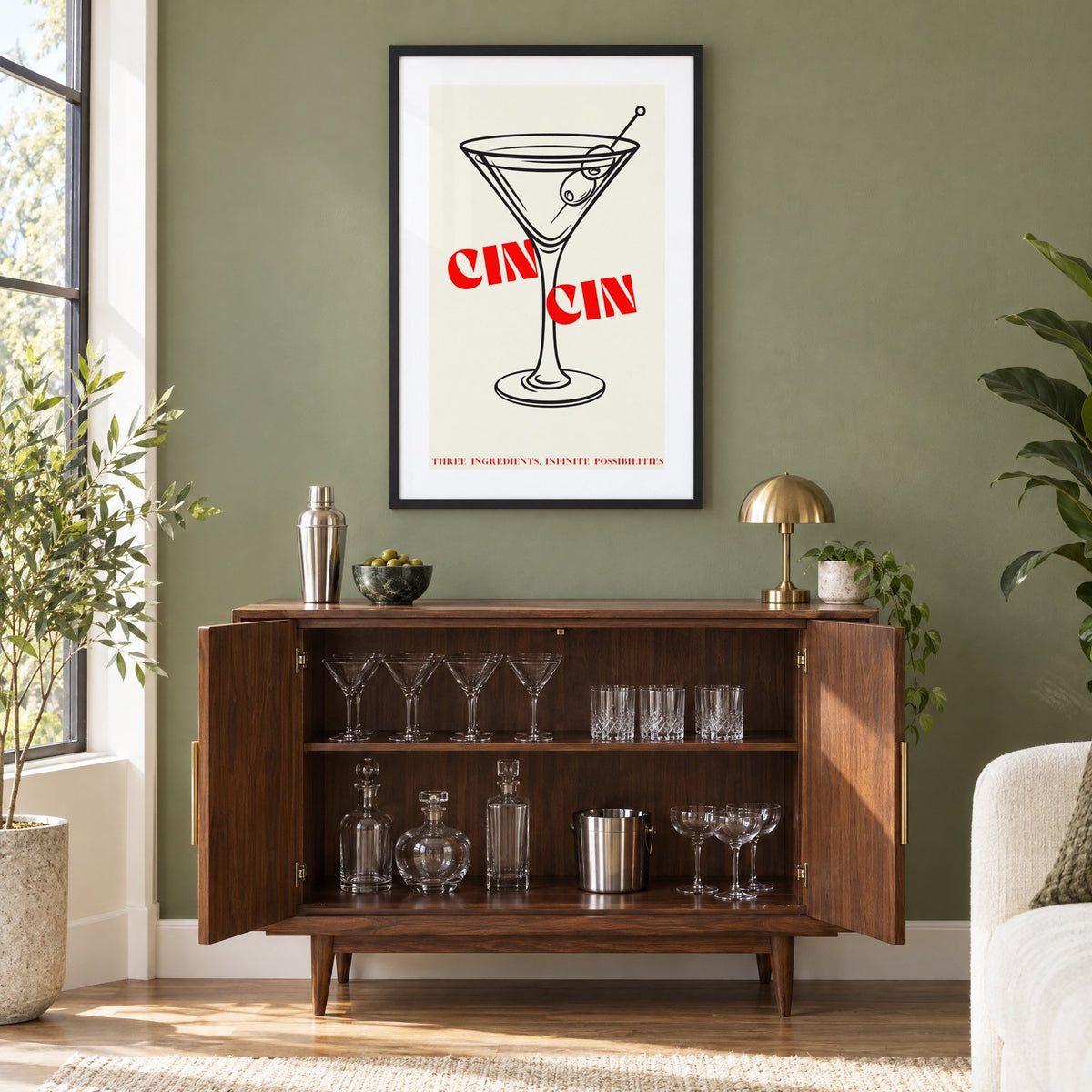 CIN CIN red type martini olives print in a black frame on an olive green wall above a walnut bar cabinet with glassware