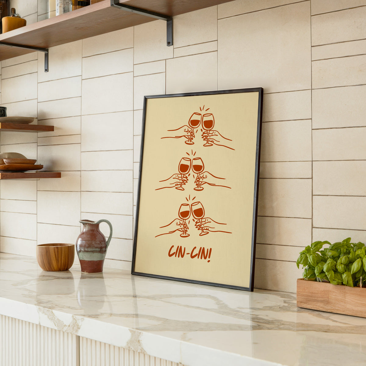 Cin Cin toasting hands print in a black frame leaning on a marble counter in a tiled kitchen