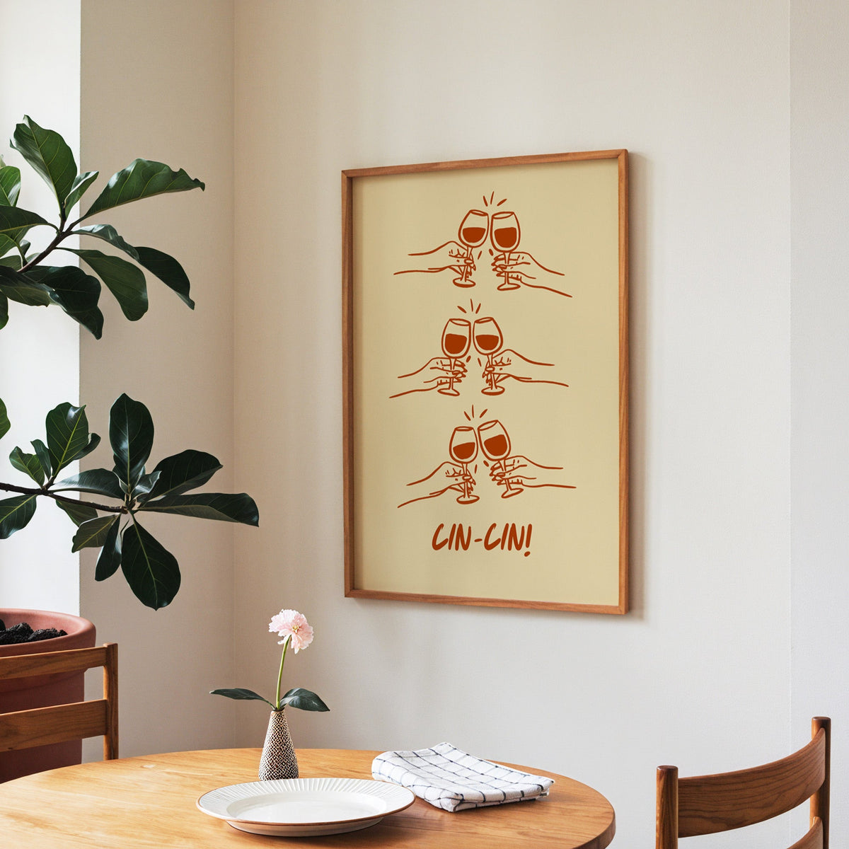 Cin Cin toasting hands print in a walnut frame above a round table beside a fiddle-leaf fig