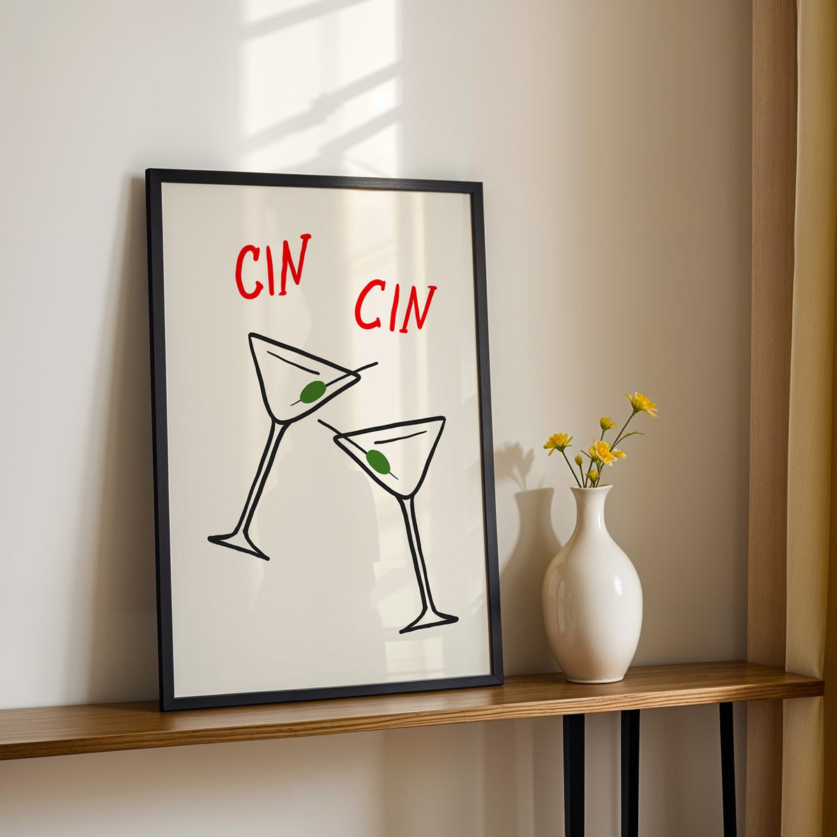 Cin cin olive martini print in a black frame on a console with yellow daisies