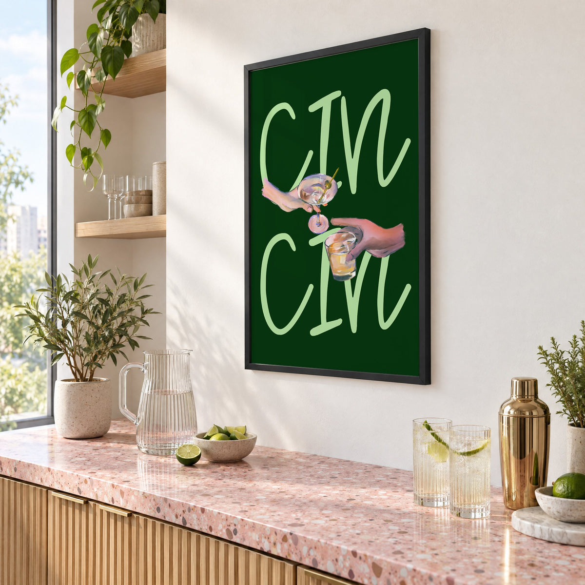 CIN CIN martini and whiskey toast print in a black frame above a pink terrazzo cocktail counter with limes, seen at an angle