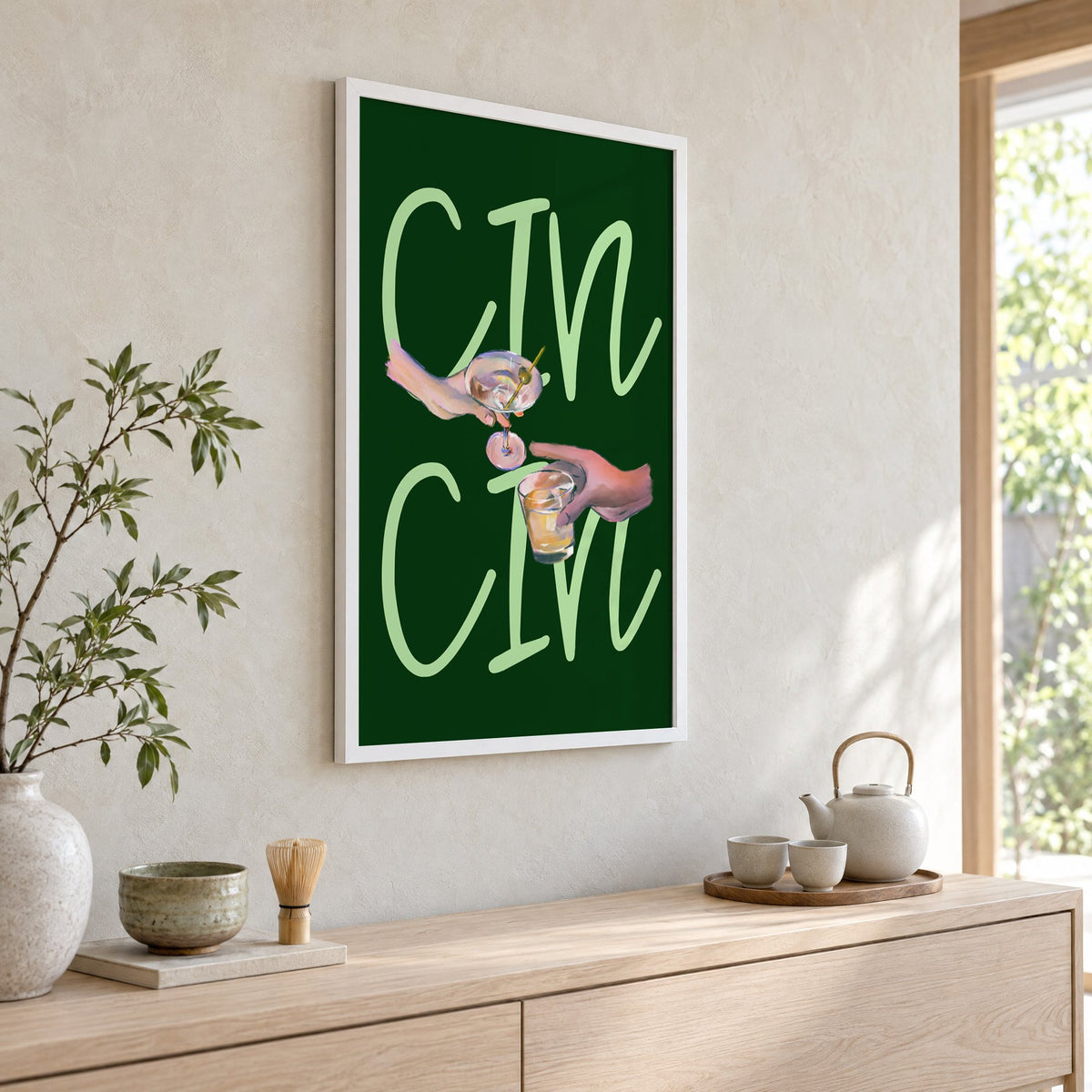 CIN CIN martini and whiskey toast print in a white frame above a pale wood console with a matcha tea set