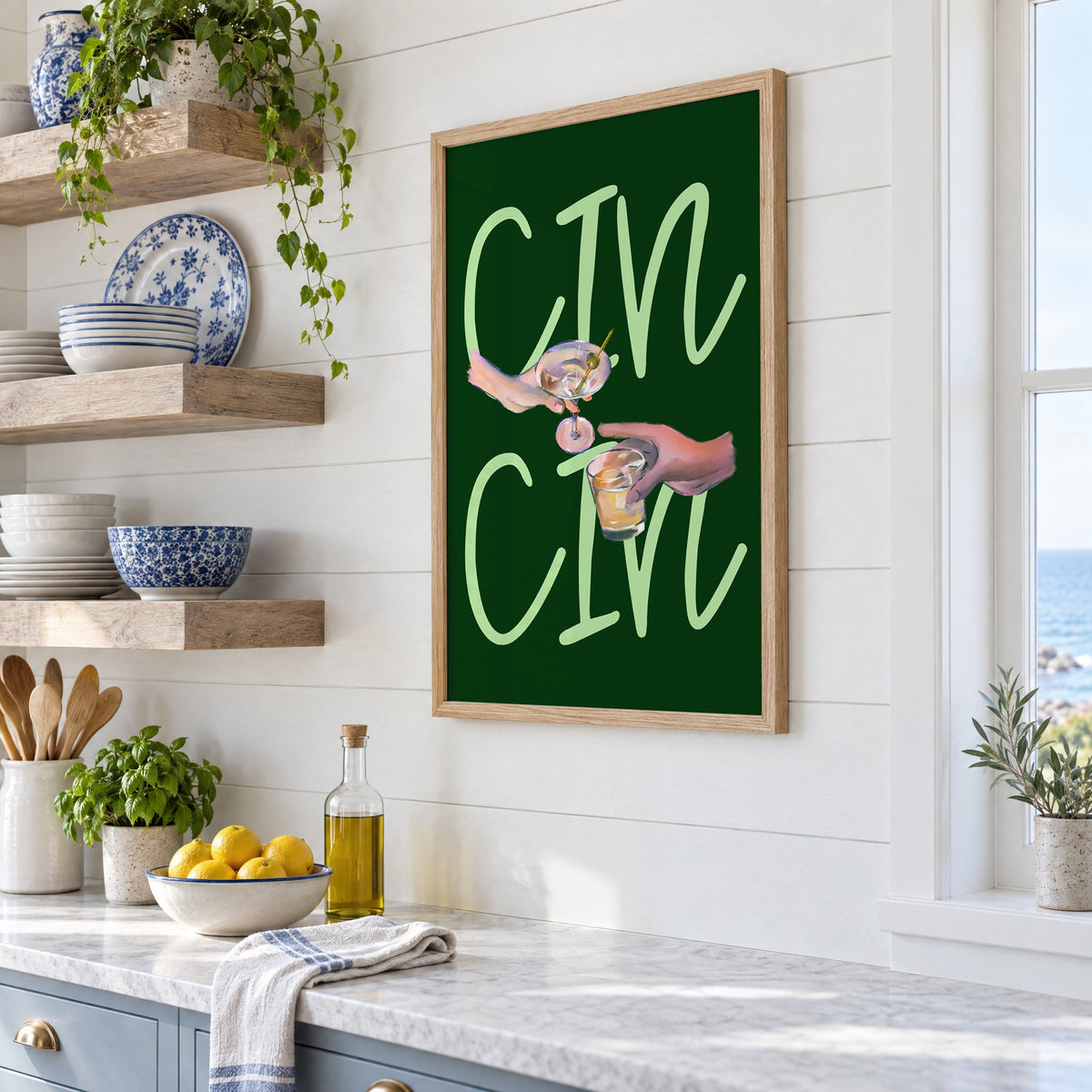 CIN CIN martini and whiskey toast print in an oak frame in a white coastal kitchen beside blue and white plates
