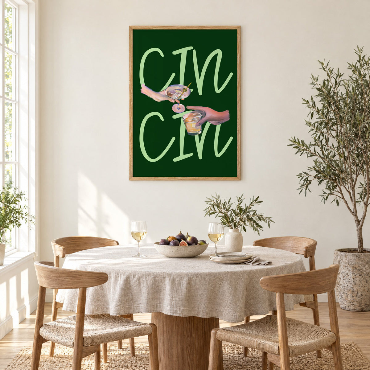 CIN CIN martini and whiskey toast print in an oak frame above a round linen-covered dining table with figs and wine