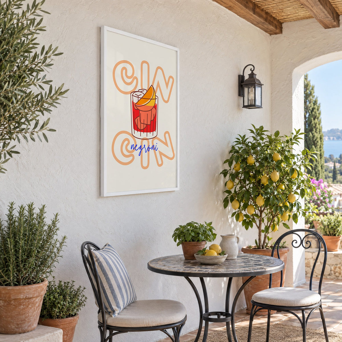 Cin Cin negroni orange slice print in a white frame on a sunny patio wall beside a potted lemon tree