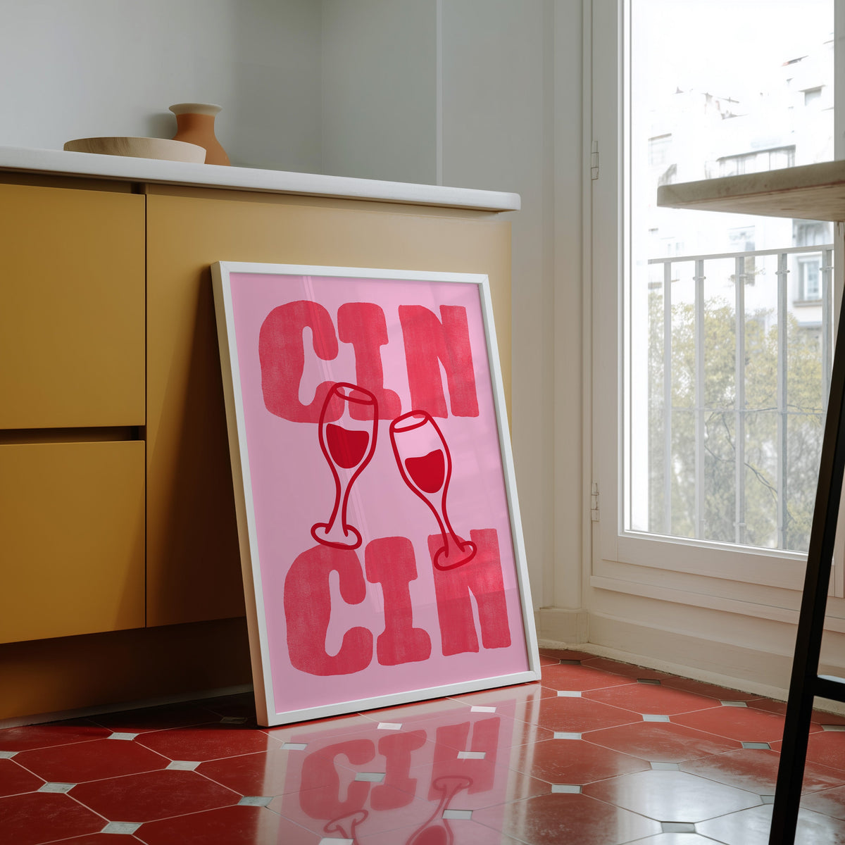 Cin Cin pink type print in a white frame against yellow cabinets on a red tiled floor