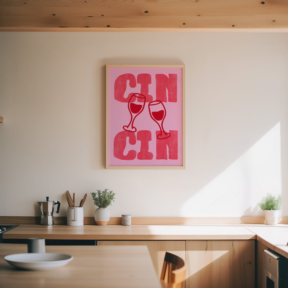 Cin Cin pink type print in an oak frame above a wood counter with a moka pot and herbs