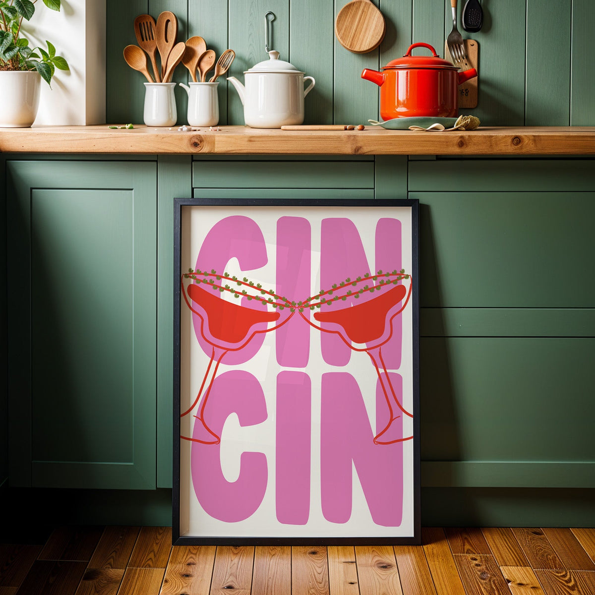 Cin cin pink coupe print in a black frame against sage green kitchen cabinets