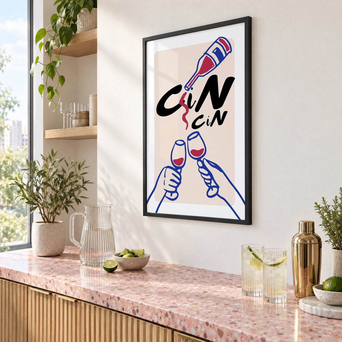 CiN CiN red wine toast print in a black frame above a pink terrazzo cocktail counter with limes, seen at an angle