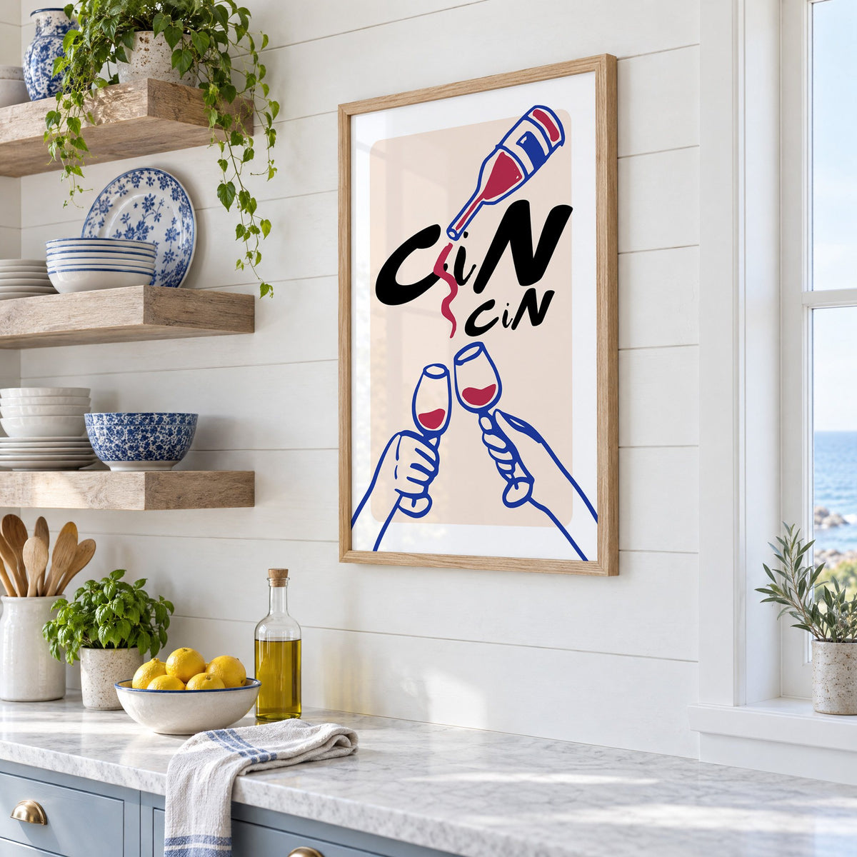CiN CiN red wine toast print in an oak frame in a white coastal kitchen beside blue and white plates