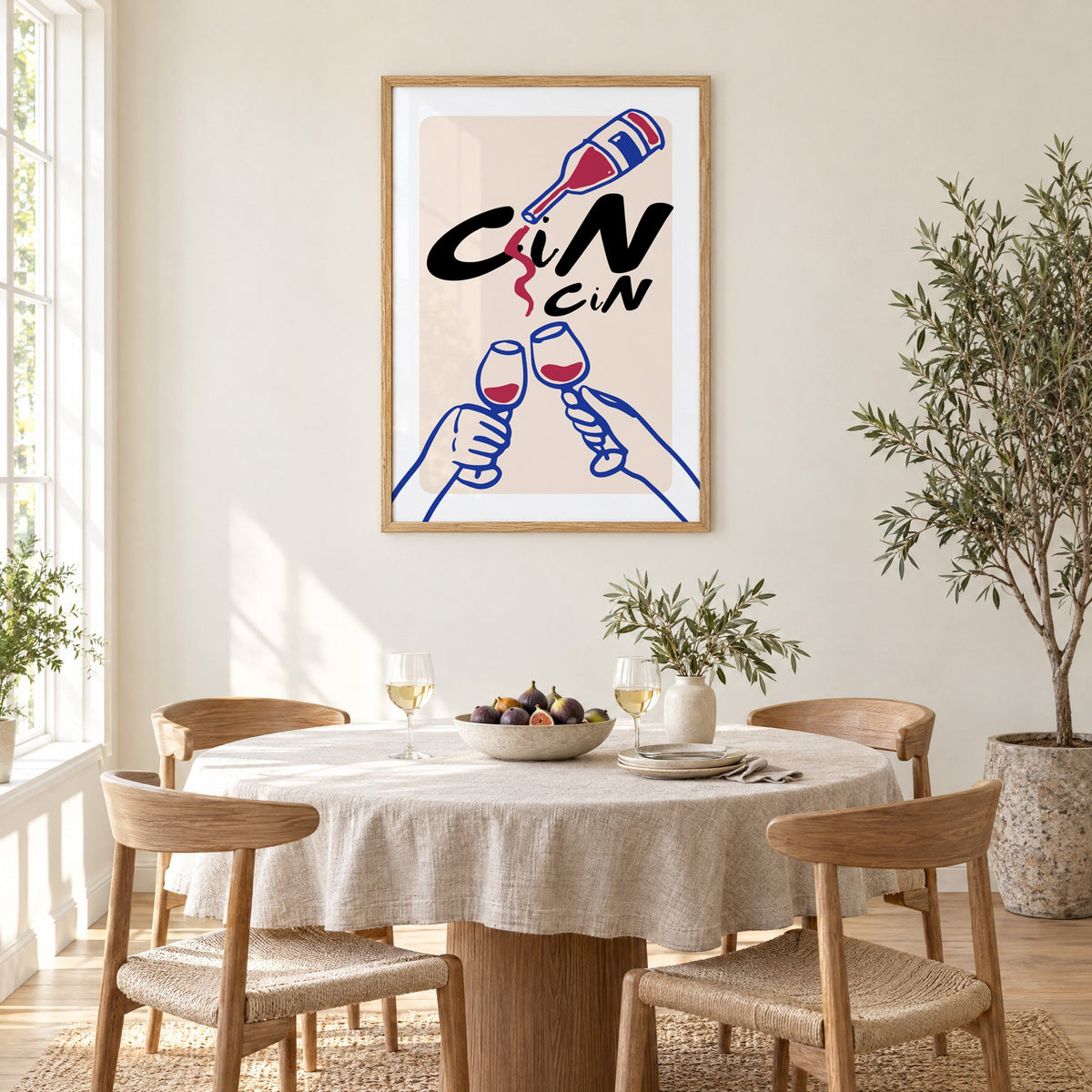 CiN CiN red wine toast print in an oak frame above a round linen-covered dining table with figs and wine