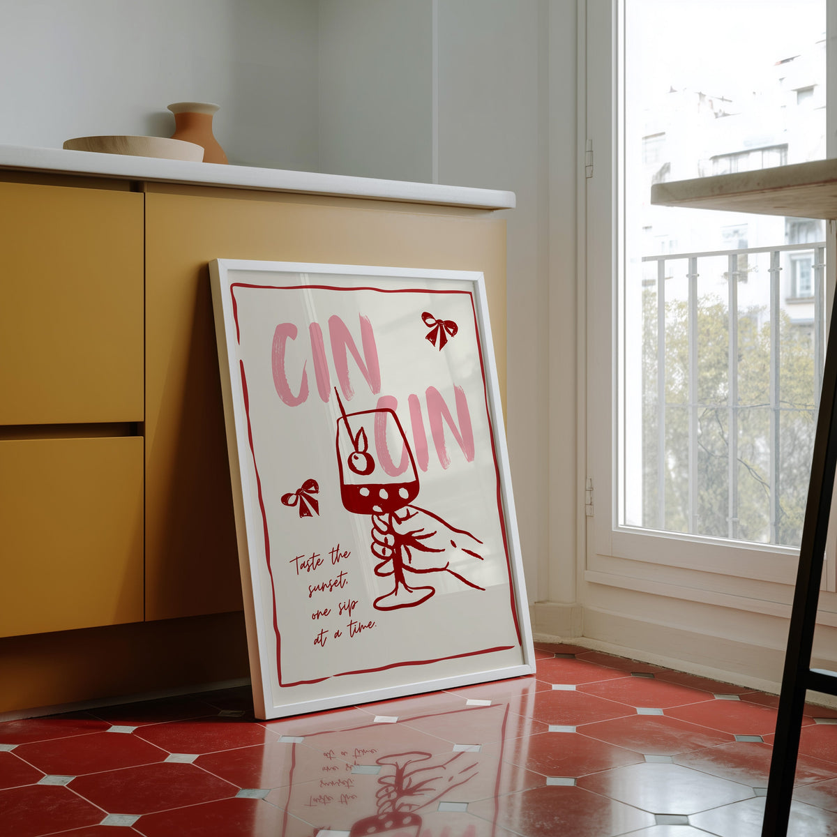 Cin Cin wine print in a white frame against yellow cabinets on a red tiled floor