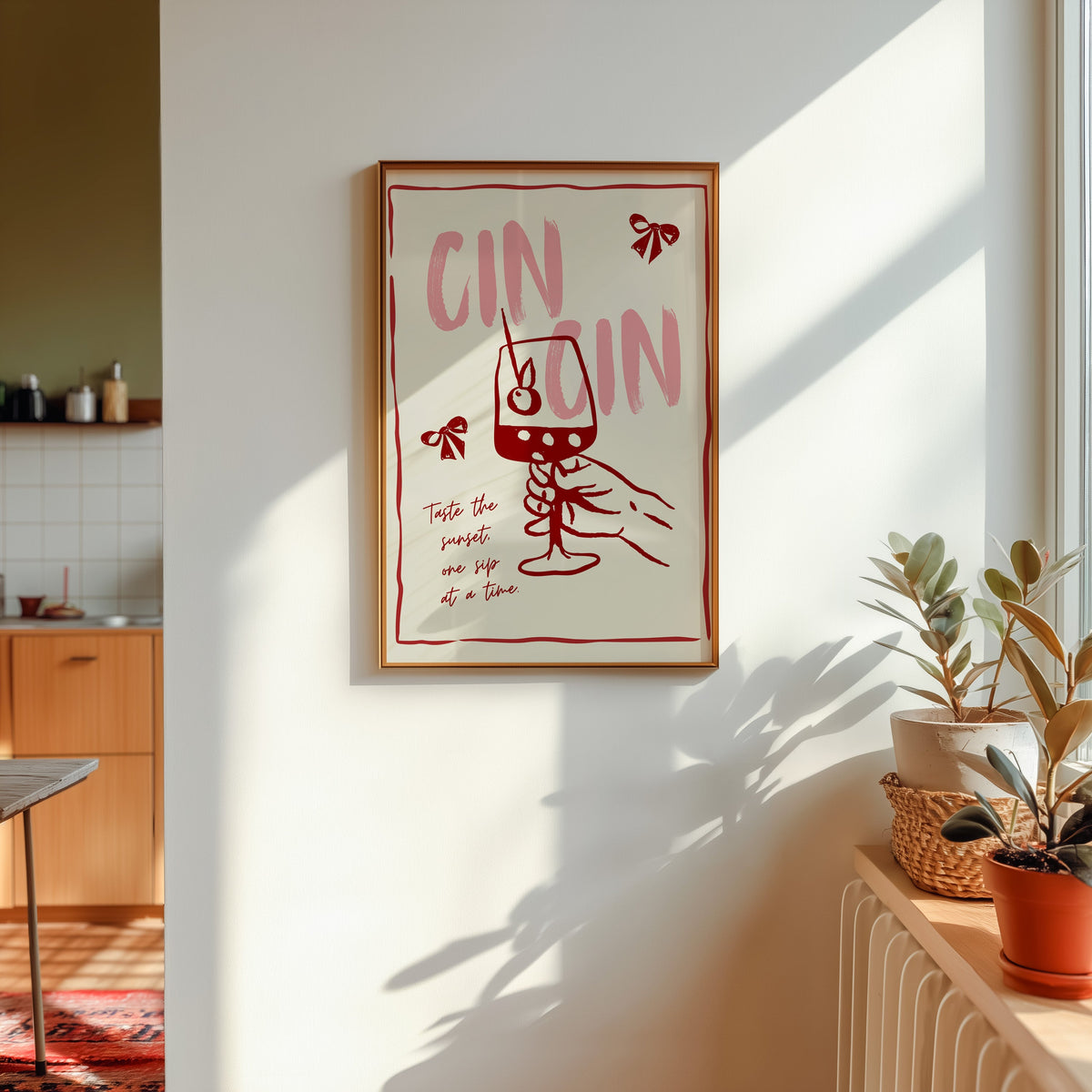 Cin Cin wine print in a gold frame in sunlight with plants on the ledge and a kitchen beyond