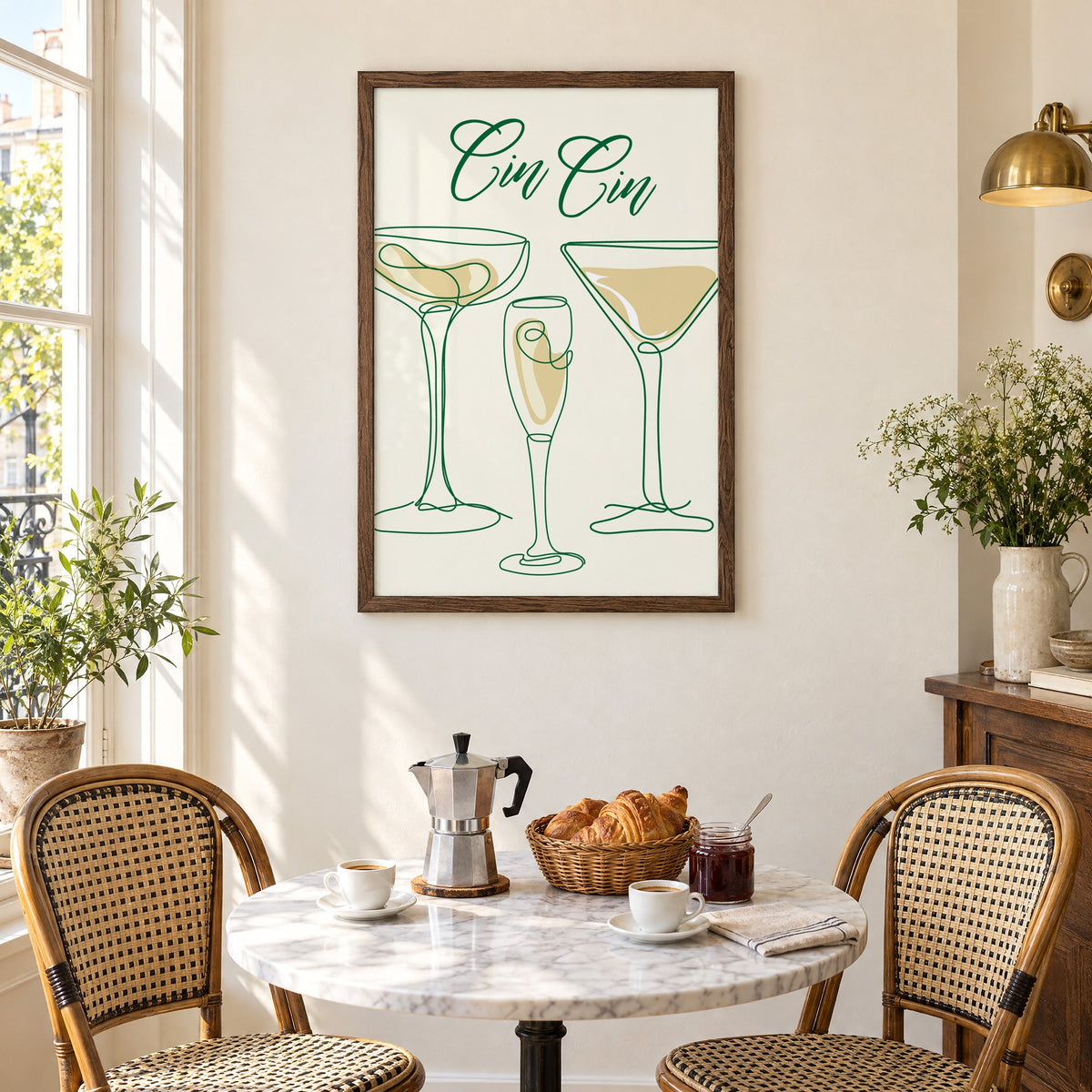 Cin Cin one-line coupe, flute and martini print in a walnut frame above a marble bistro table with croissants and rattan chairs