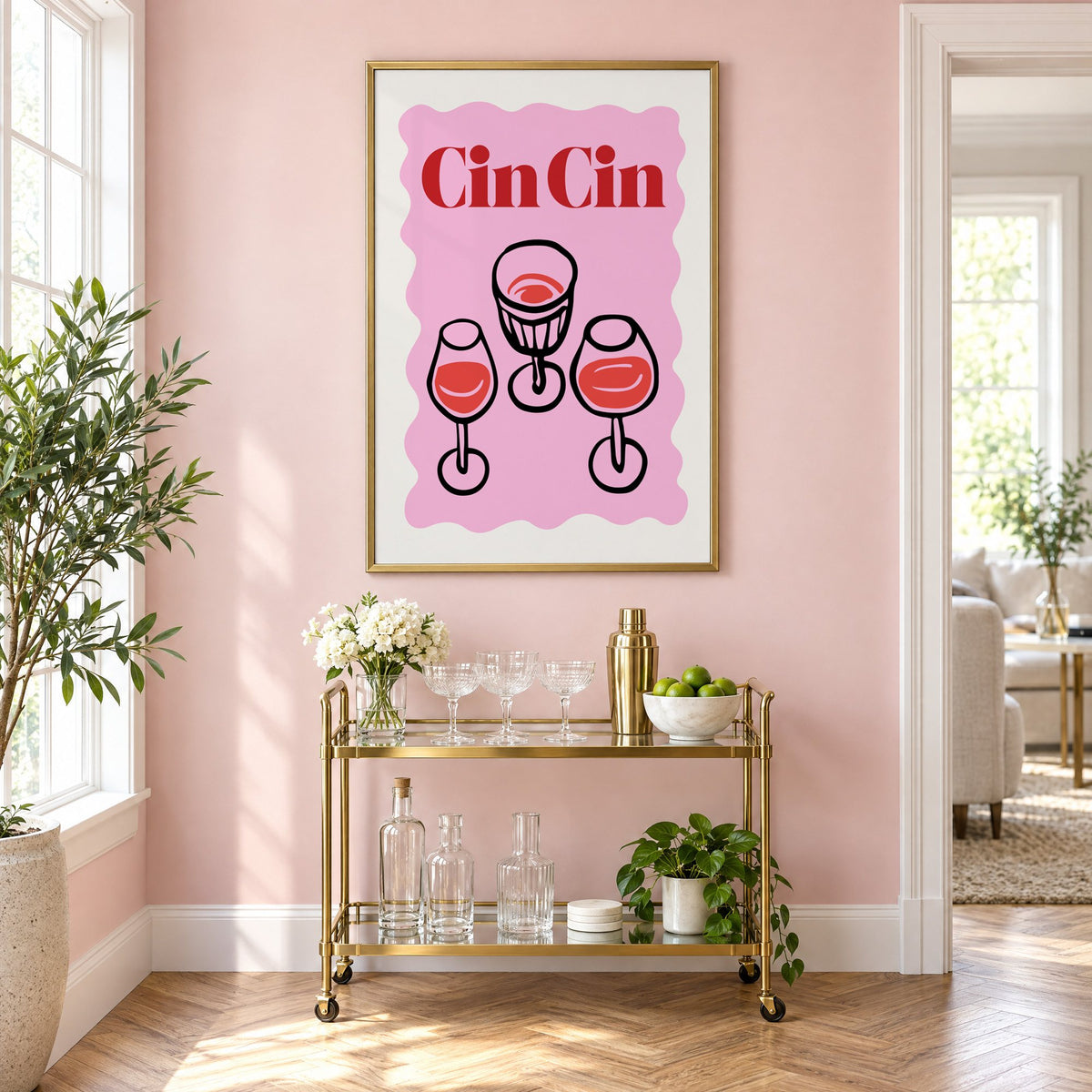 Cin Cin three glasses top view print in a brass frame on a blush pink wall above a gold bar cart with glassware