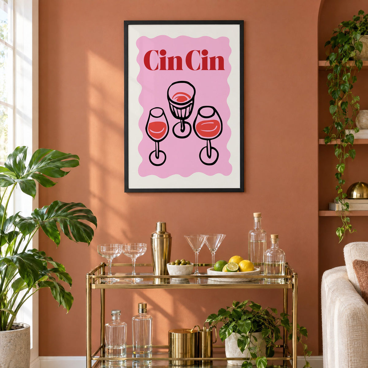 Cin Cin three glasses top view print in a black frame on a terracotta wall above a brass bar cart with coupes and citrus