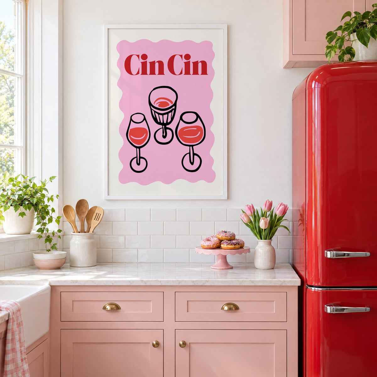 Cin Cin three glasses top view print in a white frame above pink cabinets beside a red retro fridge