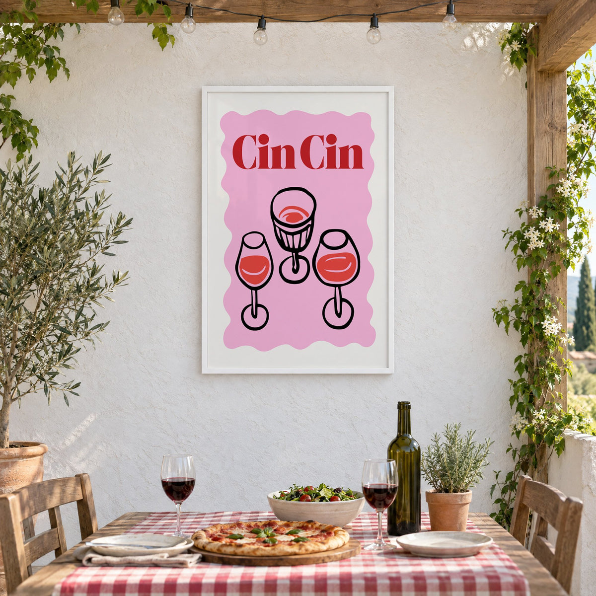 Cin Cin three glasses top view print in a white frame on a stucco wall above a checked-cloth table with pizza and red wine