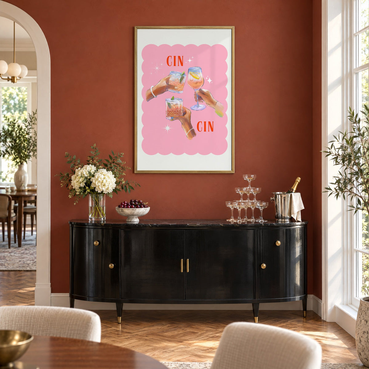 Cin Cin three hands toasting print in a brass frame on a terracotta wall above a black buffet with a champagne tower
