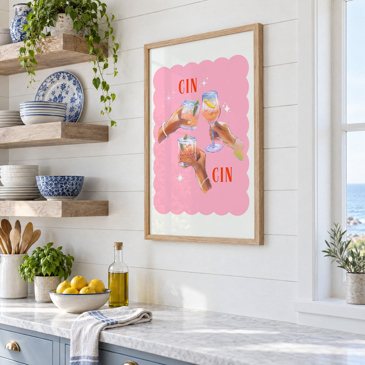 Cin Cin three hands toasting print in an oak frame in a white coastal kitchen beside blue and white plates