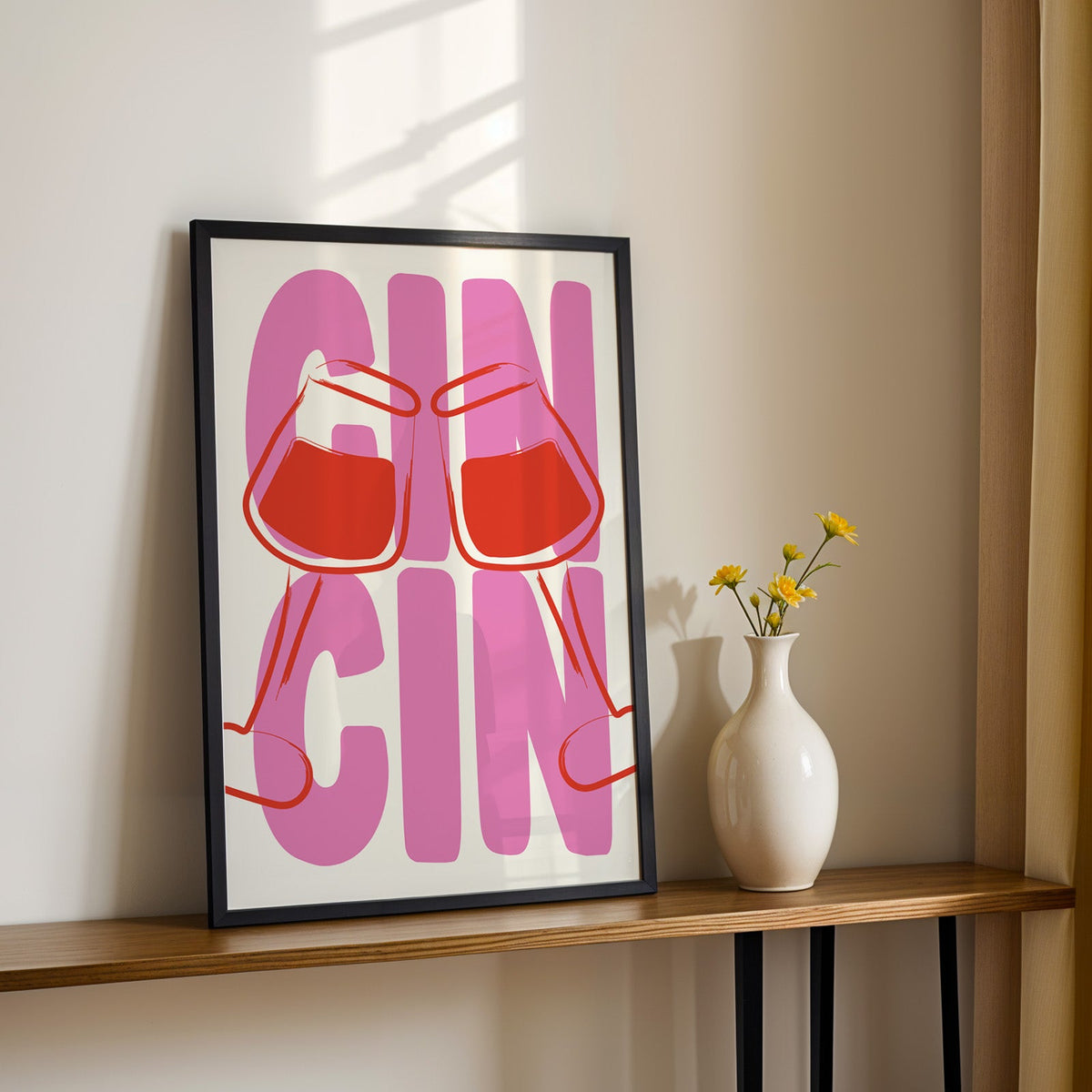 Cin cin wine glasses print in a black frame on a console table with yellow daisies