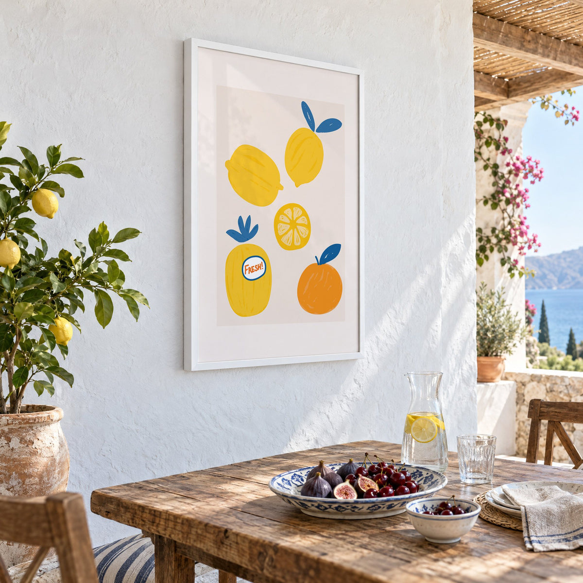 FRESH! sticker lemons and orange print in a white frame on a whitewashed terrace wall above a lunch table with figs and cherries, seen at an angle
