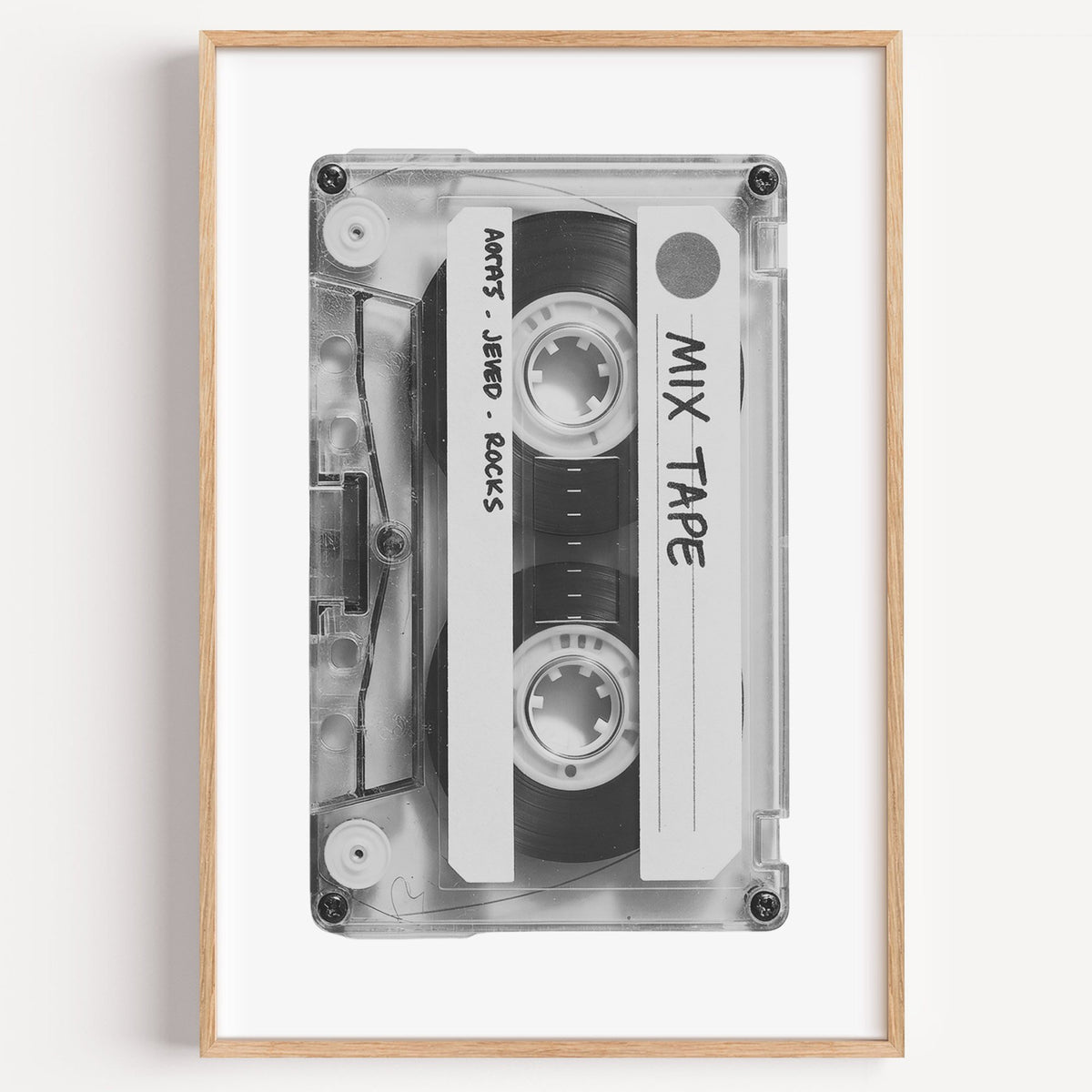 Clear mix tape cassette with handwritten label print in a light oak frame on a plain white wall