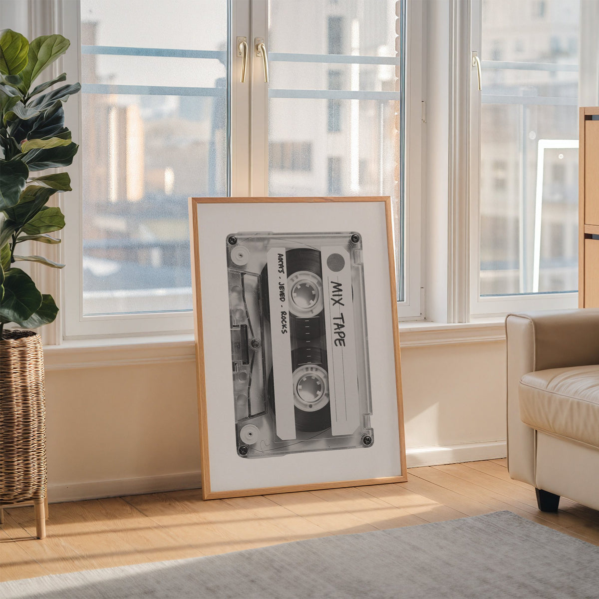Clear mix tape cassette with handwritten label print in an oak frame leaning on the floor beside a fiddle leaf fig