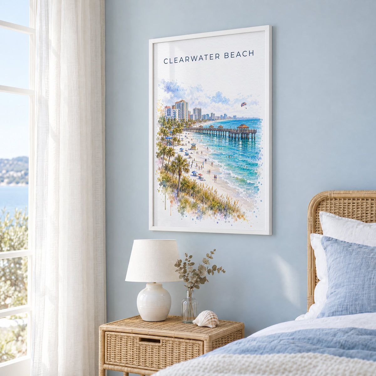 Clearwater Beach watercolor print in a white frame on a pale blue wall beside a rattan bed in a coastal bedroom
