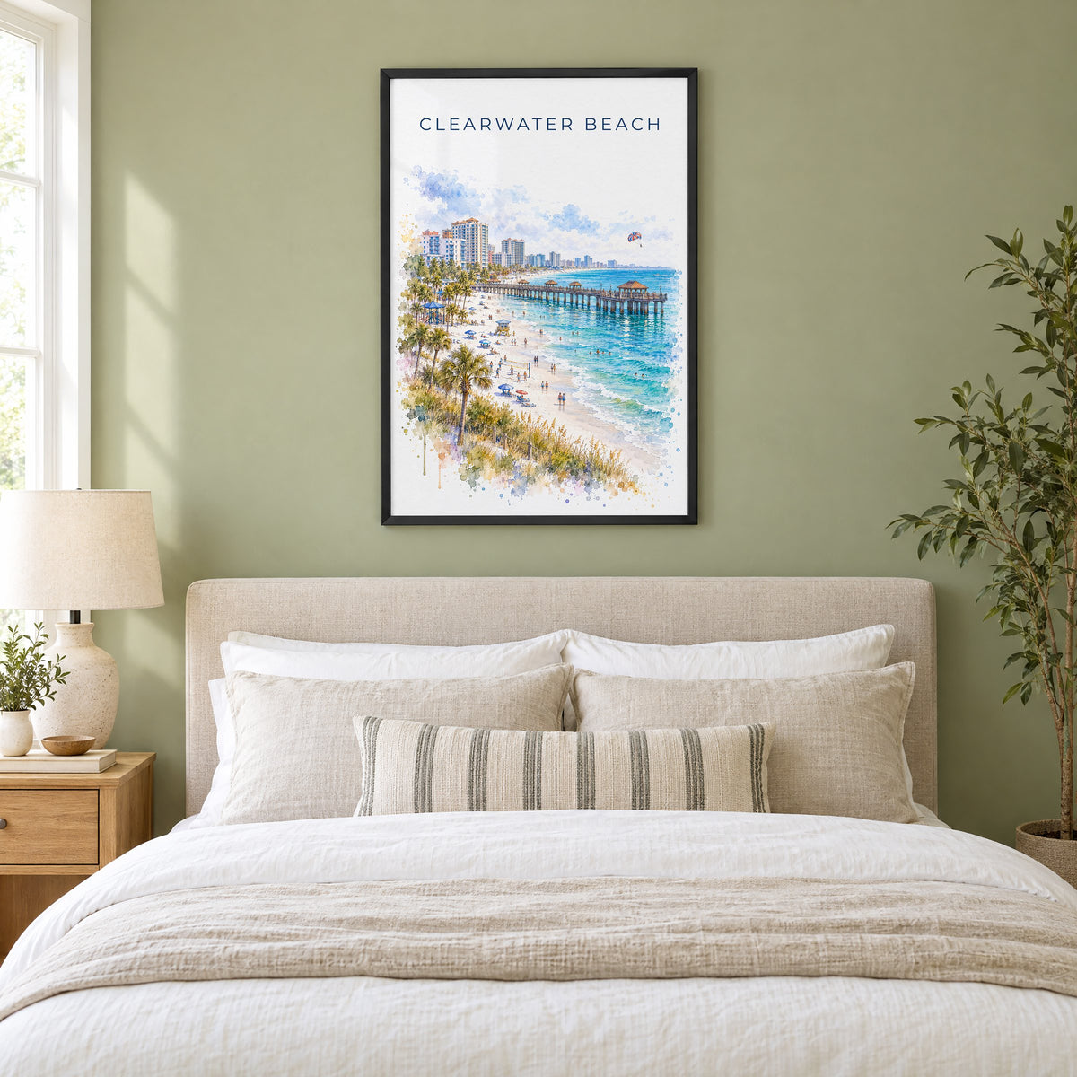 Clearwater Beach watercolor print in a black frame above an upholstered headboard in a sage green bedroom