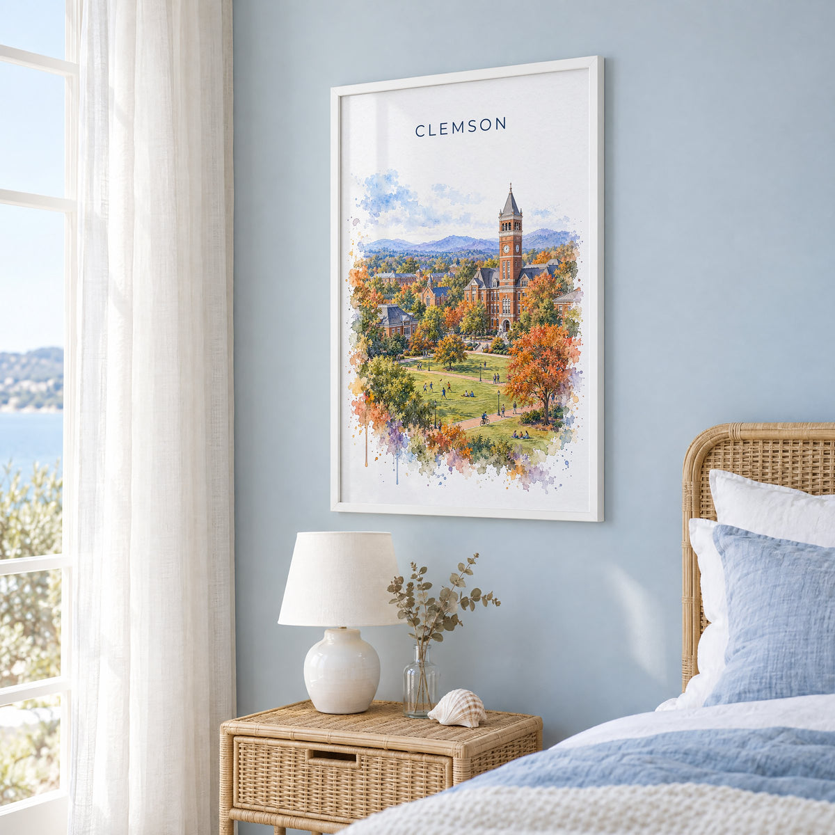 Clemson watercolor print in a white frame on a pale blue wall beside a rattan bed in a coastal bedroom