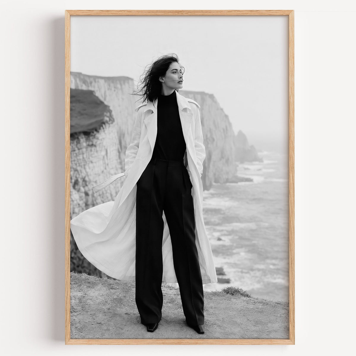 Black and white model in white trench on cliffs print in a light oak frame on a plain white wall