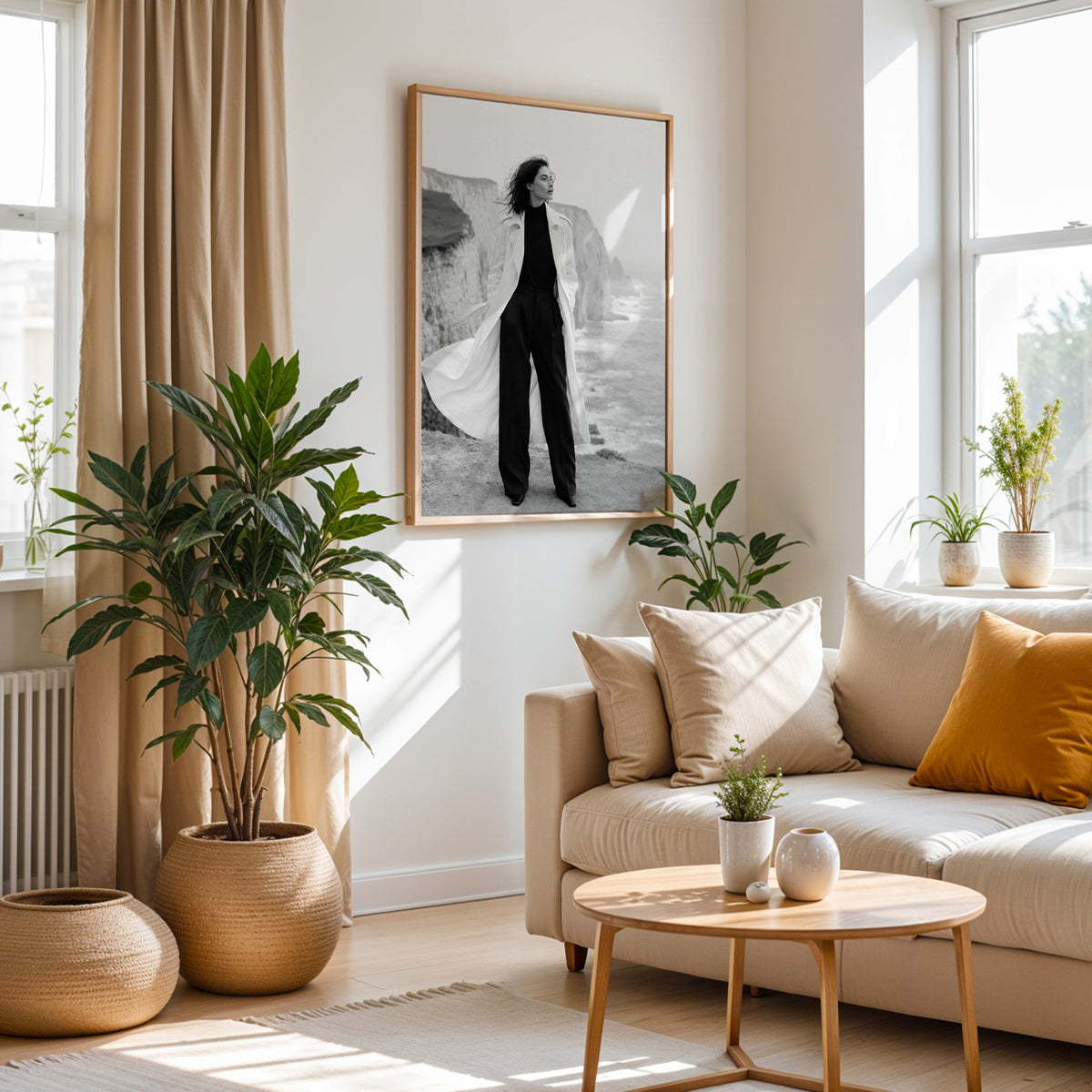 Black and white model in white trench on cliffs print in an oak frame above a cream sofa beside woven planters