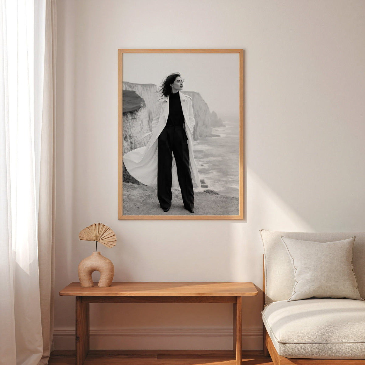 Black and white model in white trench on cliffs print in an oak frame above a narrow console with an arched vase