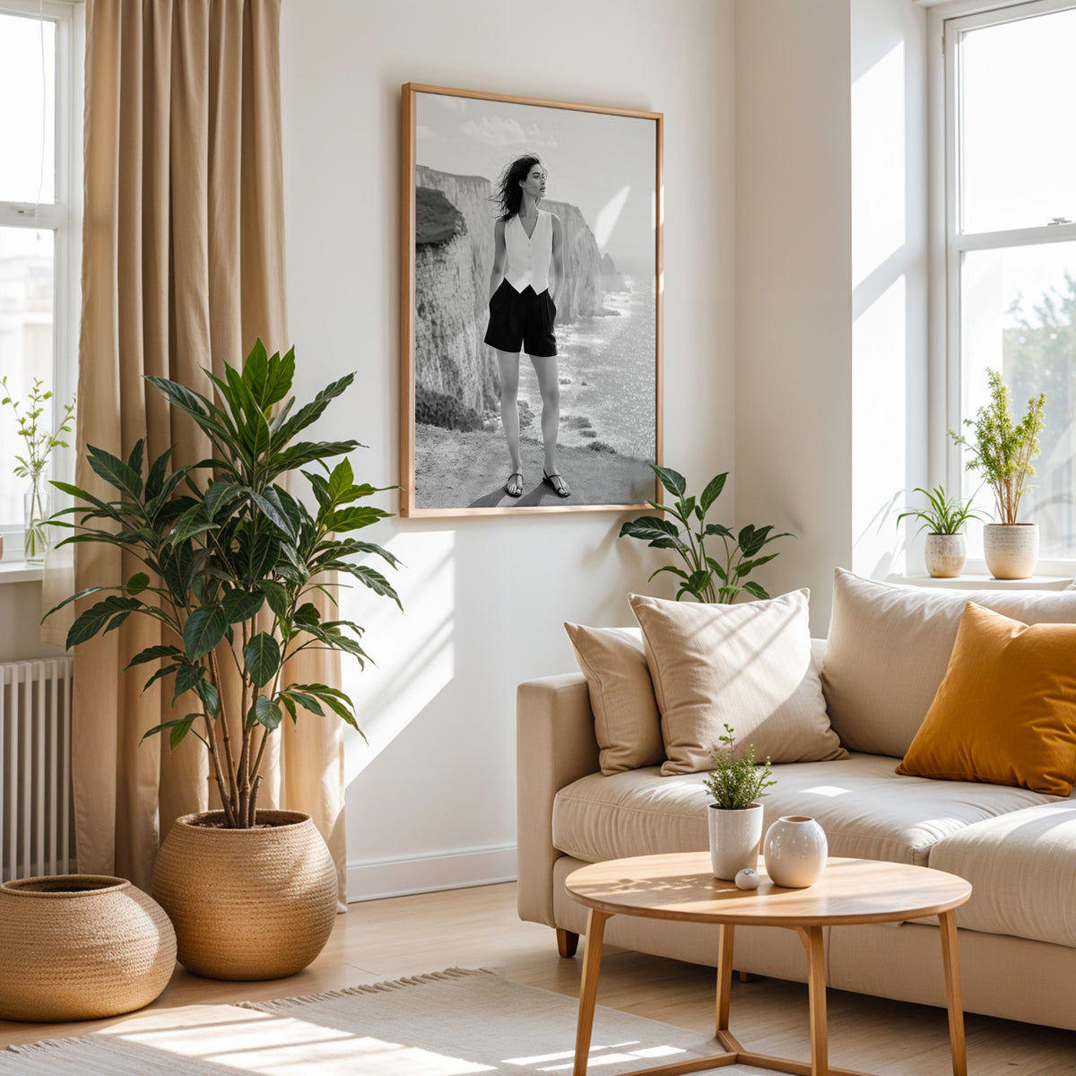 Black and white model in white vest on cliffs print in an oak frame above a cream sofa beside woven planters