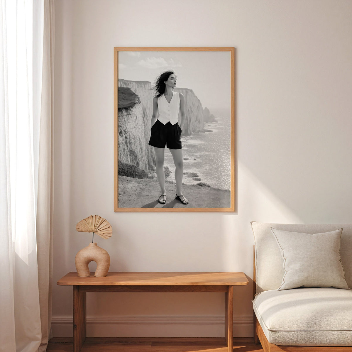 Black and white model in white vest on cliffs print in an oak frame above a narrow console with an arched vase