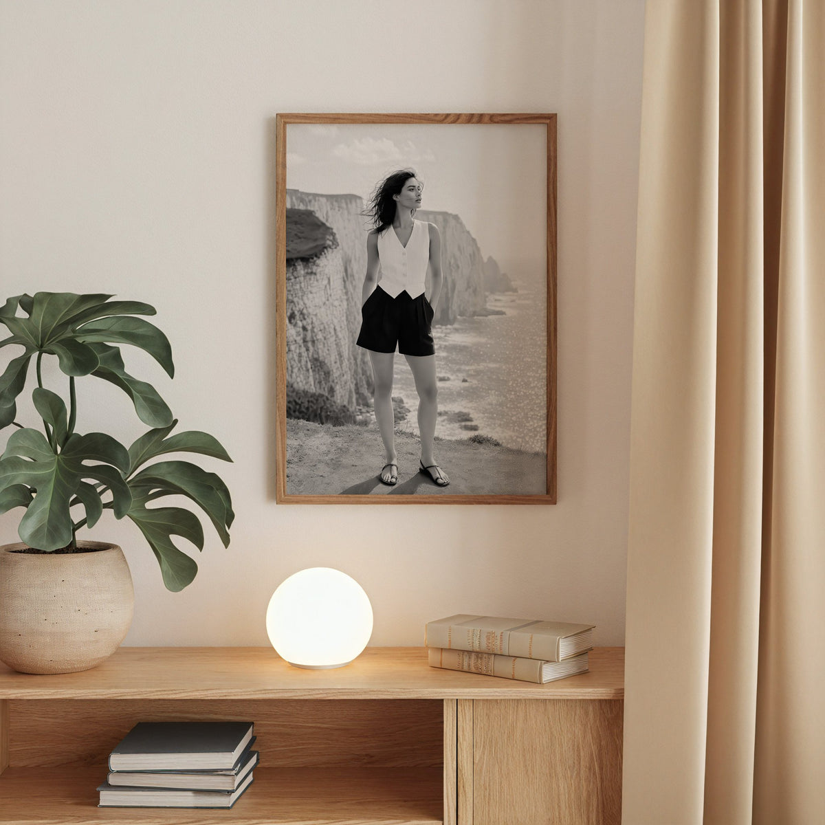 Black and white model in white vest on cliffs print in a walnut frame above an oak cabinet with a glowing globe lamp