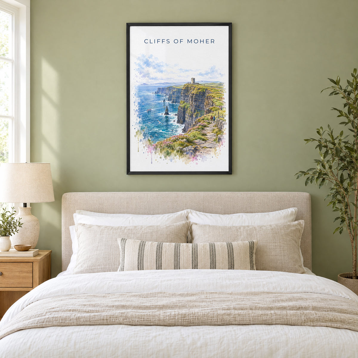 Cliffs of Moher watercolor print in a black frame above an upholstered headboard in a sage green bedroom