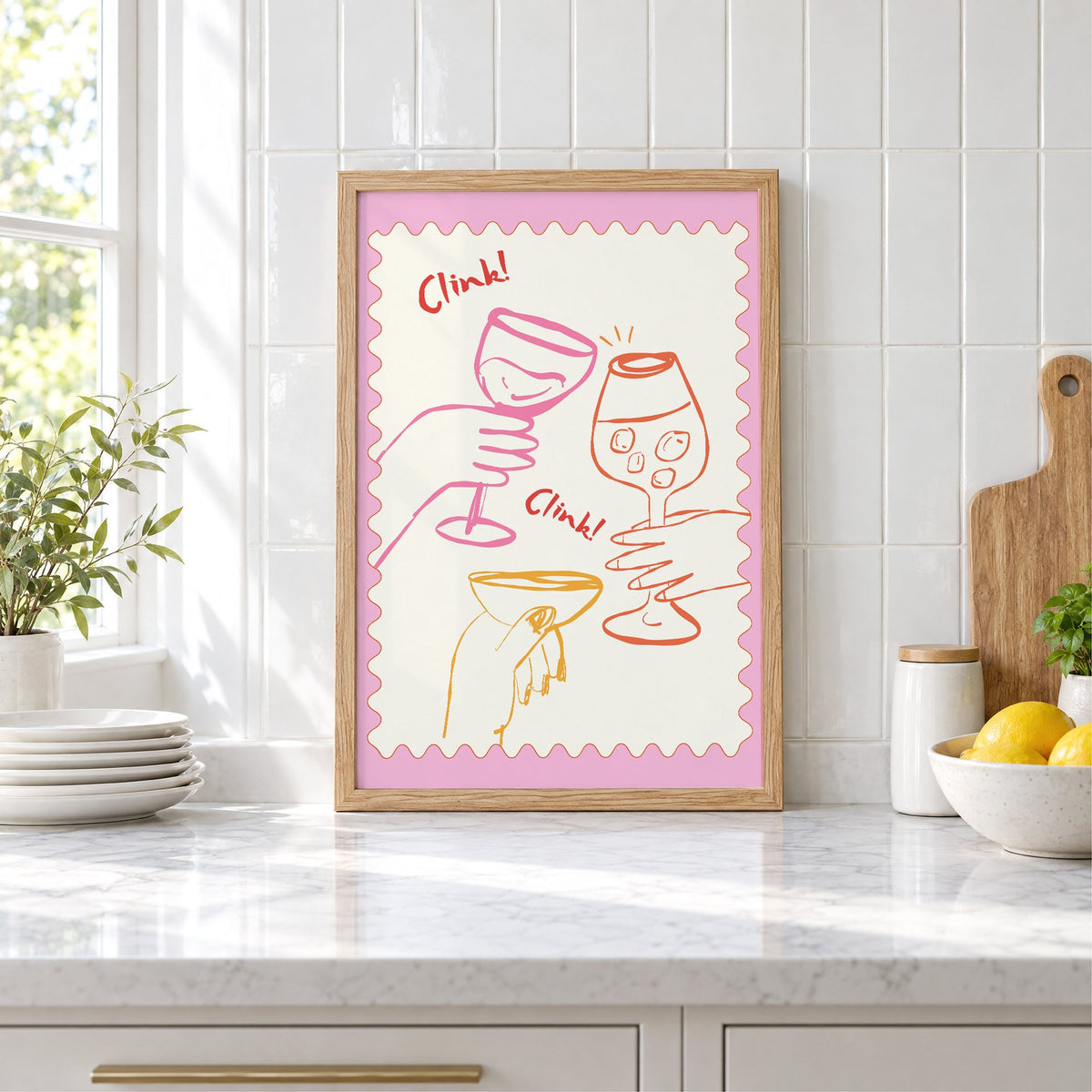 Clink Clink three glasses toast print in an oak frame leaning on a marble counter by white tiles and lemons