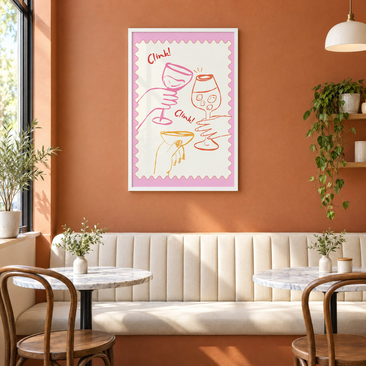 Clink Clink three glasses toast print in a white frame above a cream banquette on a terracotta cafe wall
