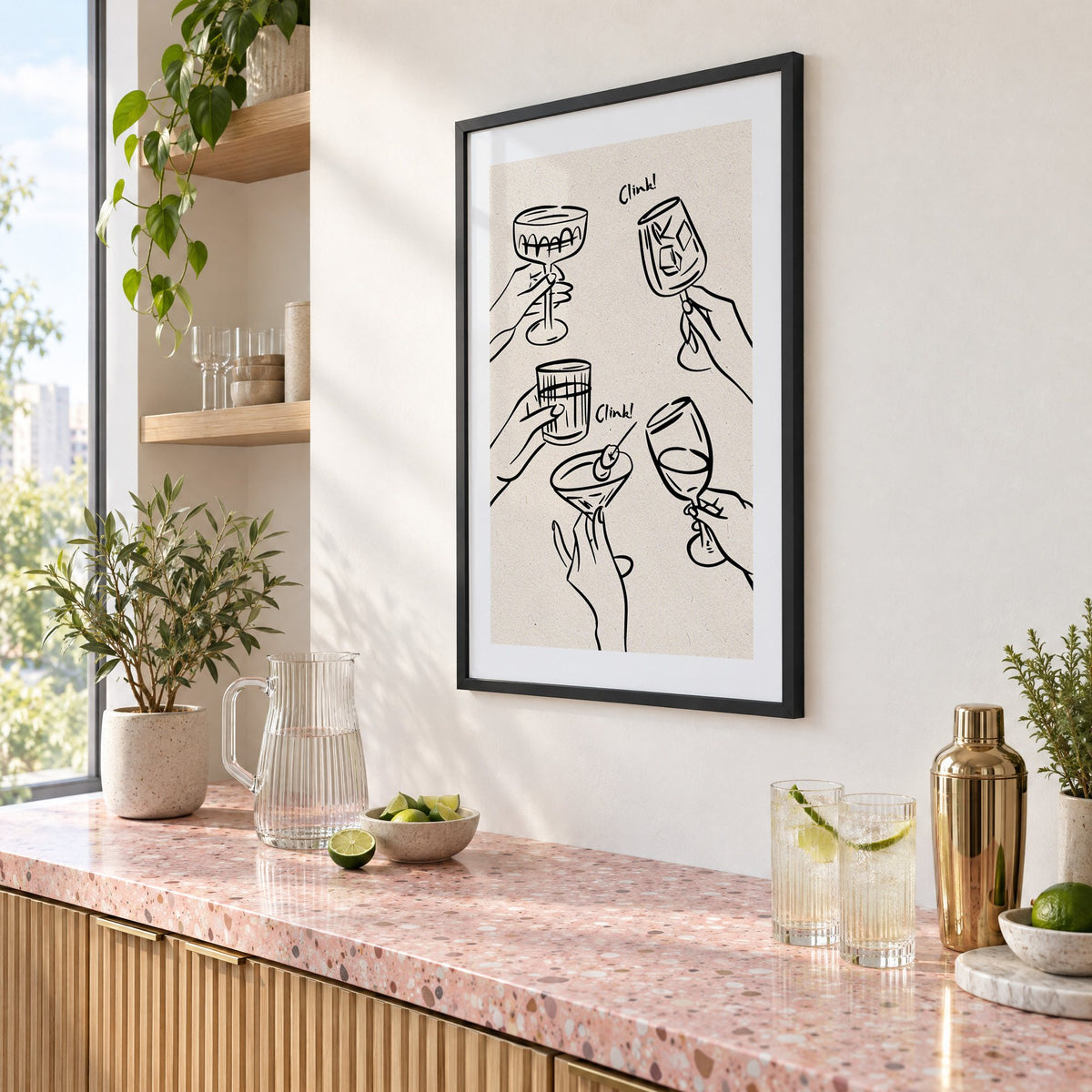 Clink! black line-art cocktail toast print in a black frame above a pink terrazzo cocktail counter with limes, seen at an angle