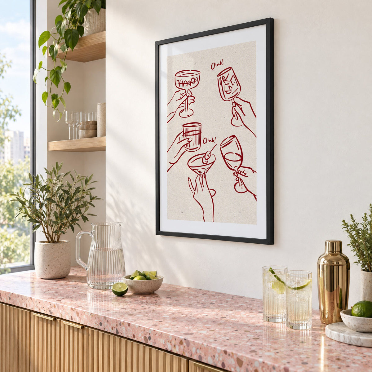 Clink! wine-red cocktail toast print in a black frame above a pink terrazzo cocktail counter with limes, seen at an angle
