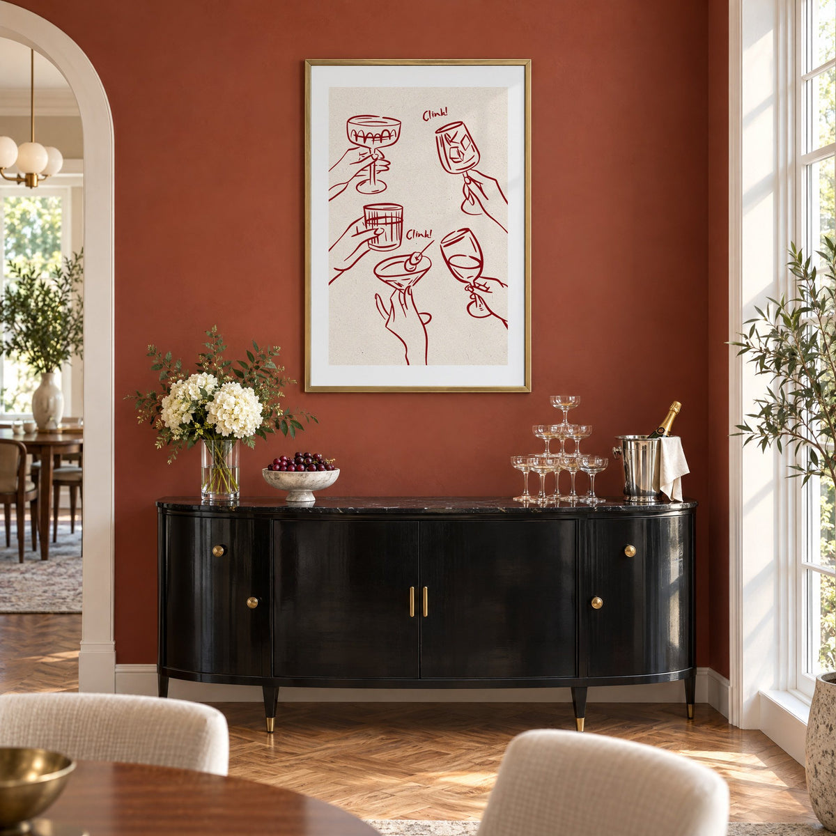 Clink! wine-red cocktail toast print in a brass frame on a terracotta wall above a black buffet with a champagne tower