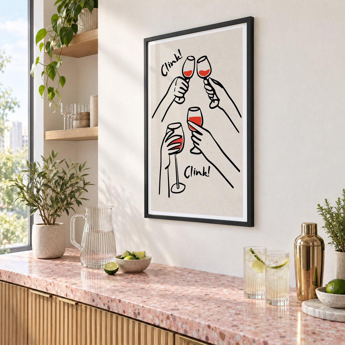 Clink! red wine toast kraft print in a black frame above a pink terrazzo cocktail counter with limes, seen at an angle