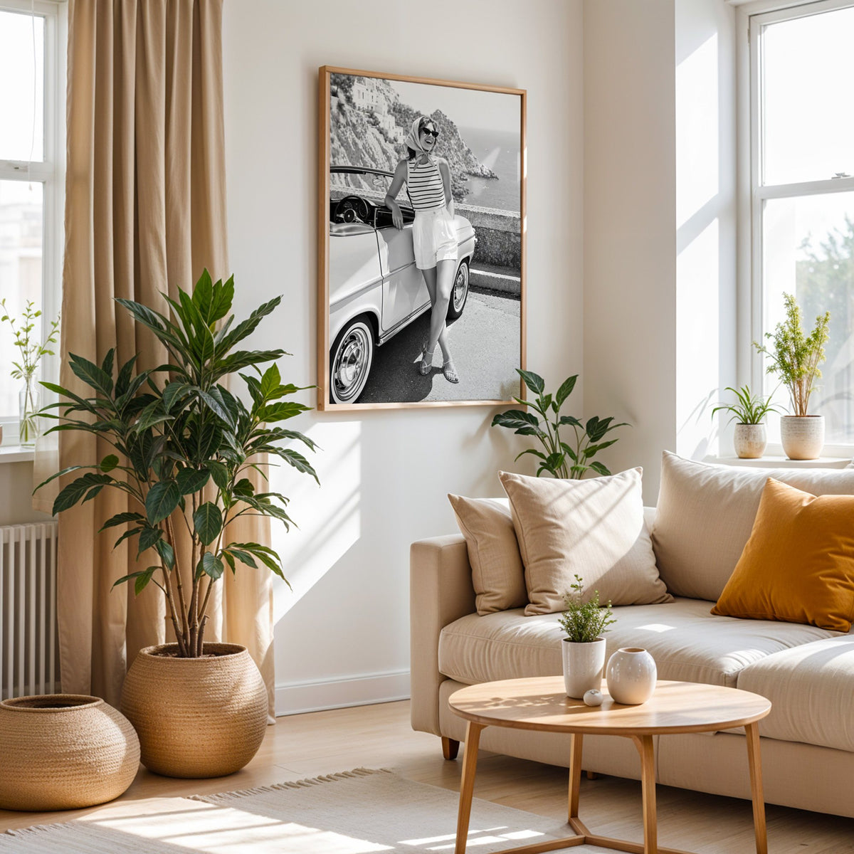 Woman leaning on vintage convertible by the sea print in an oak frame above a cream sofa beside woven planters